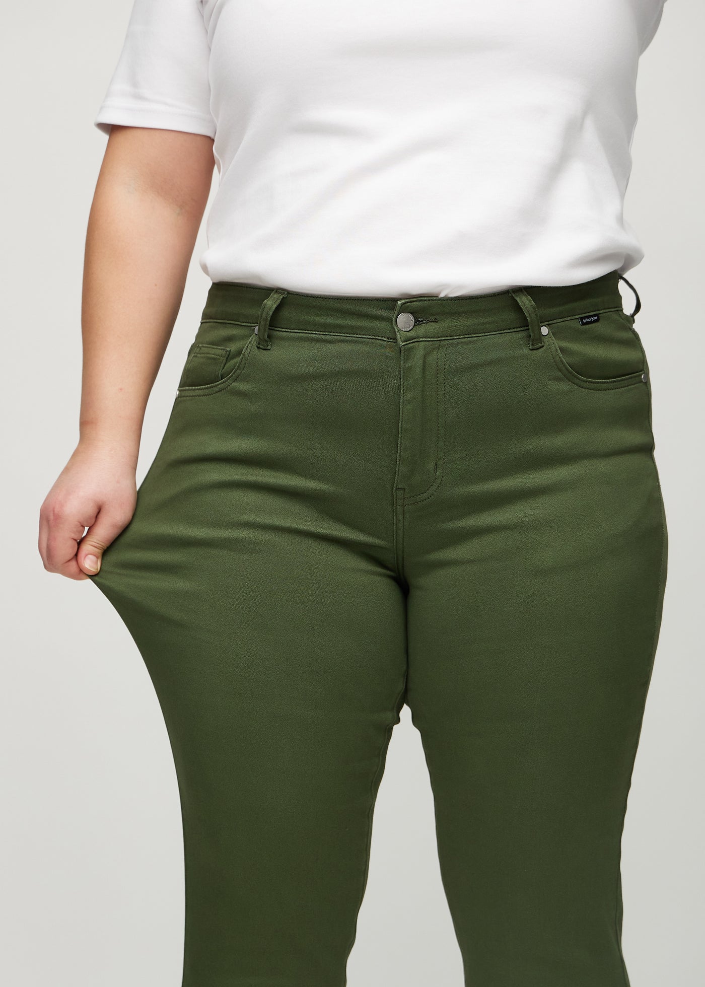 Plus-size model strækker jeansene ved låret for at vise stretch.