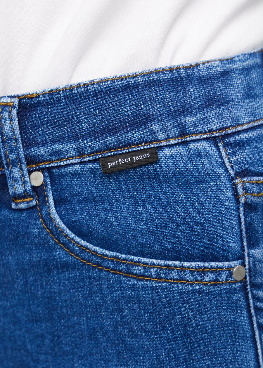 Close-up of dark blue denim with the Perfect Jeans logo label at the edge of the front pocket.