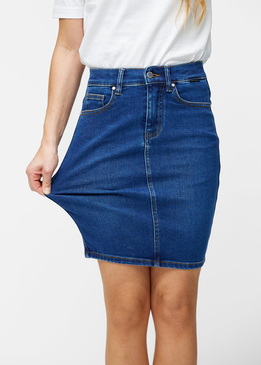 Model strækker mørkeblå, tætsiddende og knælang denimnederdel ved låret for at vise stretch.