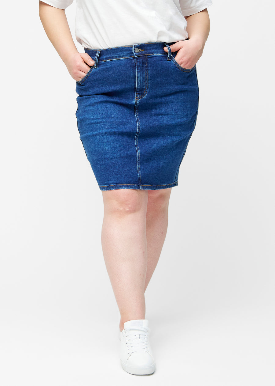 Mørkeblå, tætsiddende og knælang denimnederdel set forfra på plus-size model.