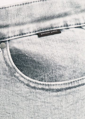Nærbillede af lysegrå denim med Perfect Jeans logoetiket ved forlommekanten.