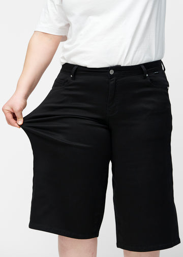 Plus-size model strækker de løse, sorte capris i farven Ravens ved hoften for at vise materialets stretch.