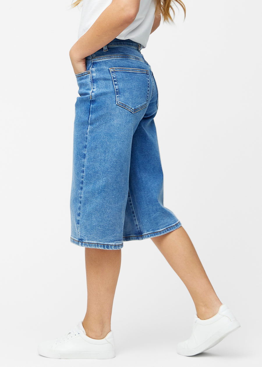 Løse, klassisk blå denim capris i farven Rivers set fra siden på model, hvor den brede pasform og længden til lige under knæet er synlig.