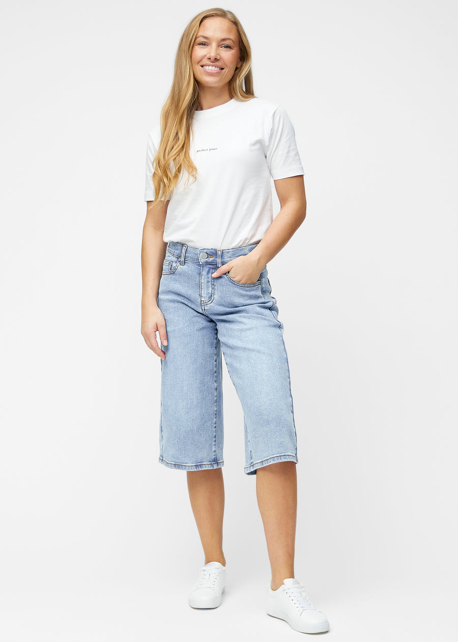 Full image of a model wearing loose, light blue denim capris in the colour Waves, reaching just below the knee.