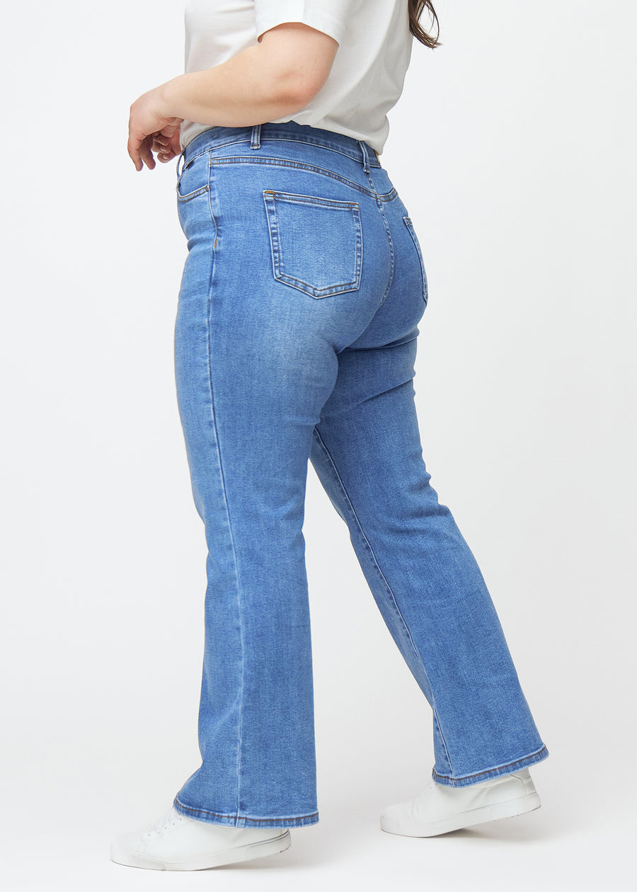 Blue mid-rise bootcut jeans in Rivers. Side view on a plus-size model.