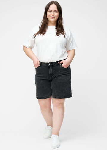 Fuldt billede af plus-size model i løse, mørkegrå denim shorts i farven Shadows, der går til lige over knæet.