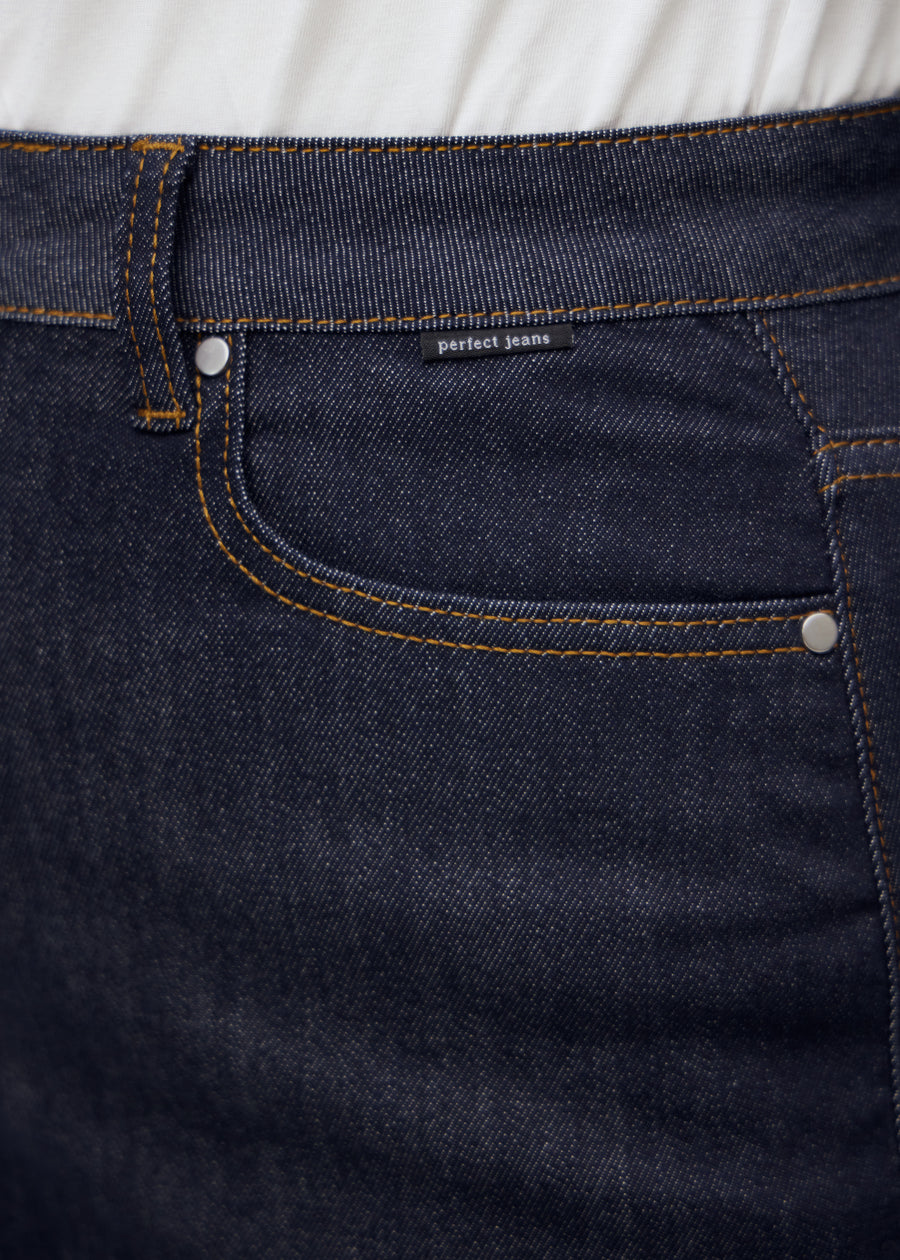 Close-up of deep dark blue denim with Perfect Jeans logo label at the front pocket edge on a plus-size model.