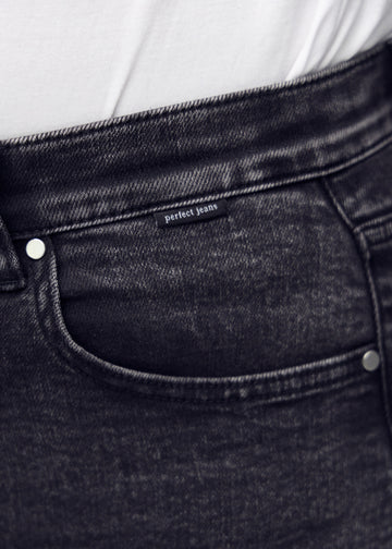 Nærbillede af mørkegrå denim med Perfect Jeans logoetiket ved forlommekanten, på plus-size model.