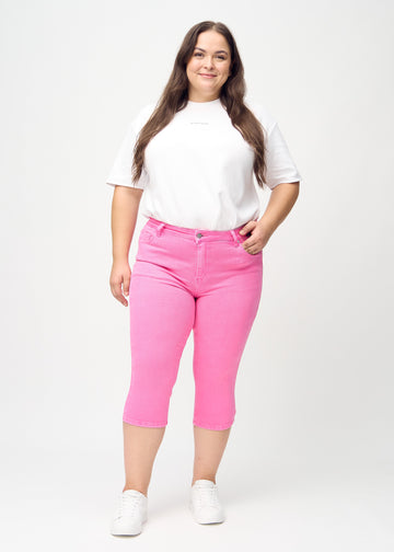 Skinny capris for women in pastel pink fabric, color Flamingos. Full-length view of a plus-size model wearing the capris.