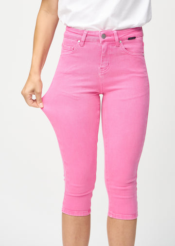 Skinny capris for women in pastel pink fabric, color Flamingos. A model stretches the fabric to demonstrate its flexibility.