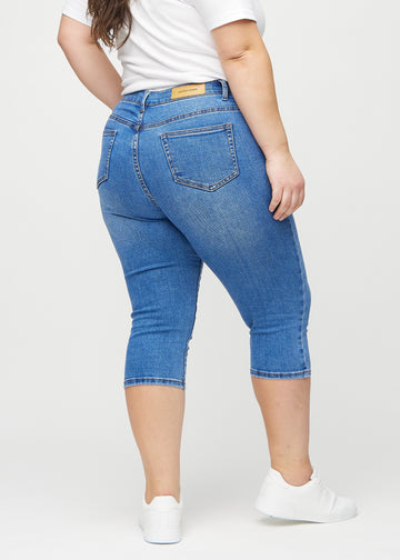 Skinny capris for women in blue denim, color Rivers. Back view on a plus-size model, showing the fit and back pockets.