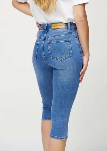 Skinny capris for women in blue denim, color Rivers. Close-up from behind on a model, highlighting pockets and stitching.