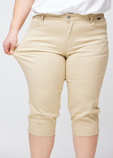 Slim capris for women in beige jeans fabric, color Gazelles. A plus-size model pulls the fabric at the thigh to demonstrate stretch and flexibility.