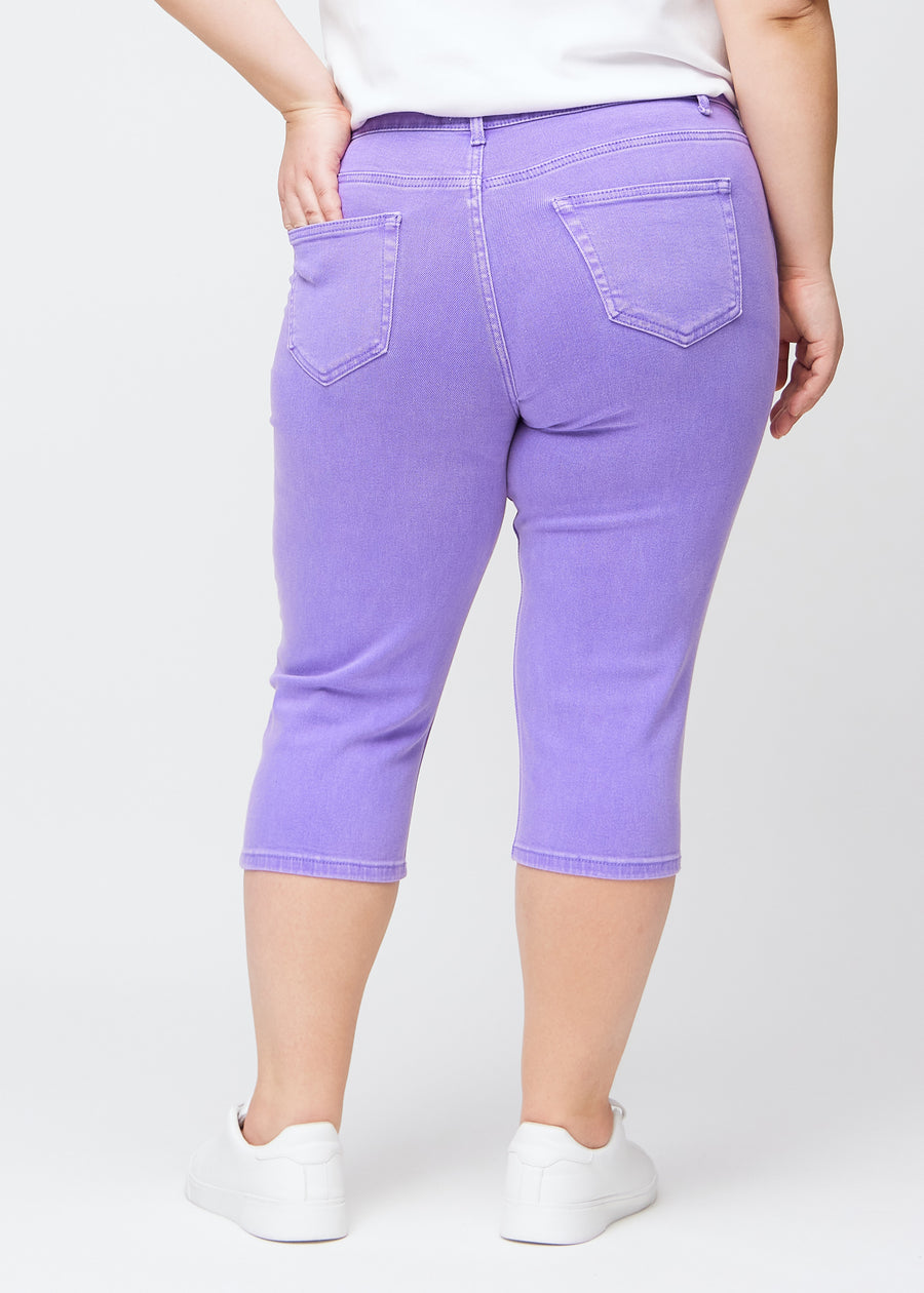 Slim capris for women in pastel purple jeans fabric, color Lavenders. Back view on a plus-size model, showing the fit, length and back pockets.