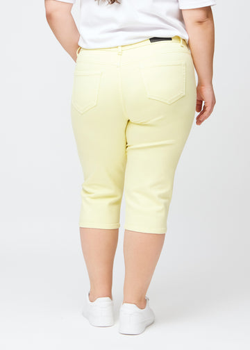 Slim capris for women in pastel light yellow jeans fabric, color Lemonades. Back view on a plus-size model, showing the fit, length and back pockets.