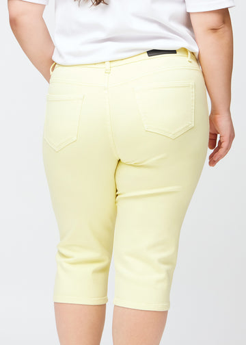 Slim capris for women in pastel light yellow jeans fabric, color Lemonades. Close-up from behind on a plus-size model, highlighting the back pockets and stitching.