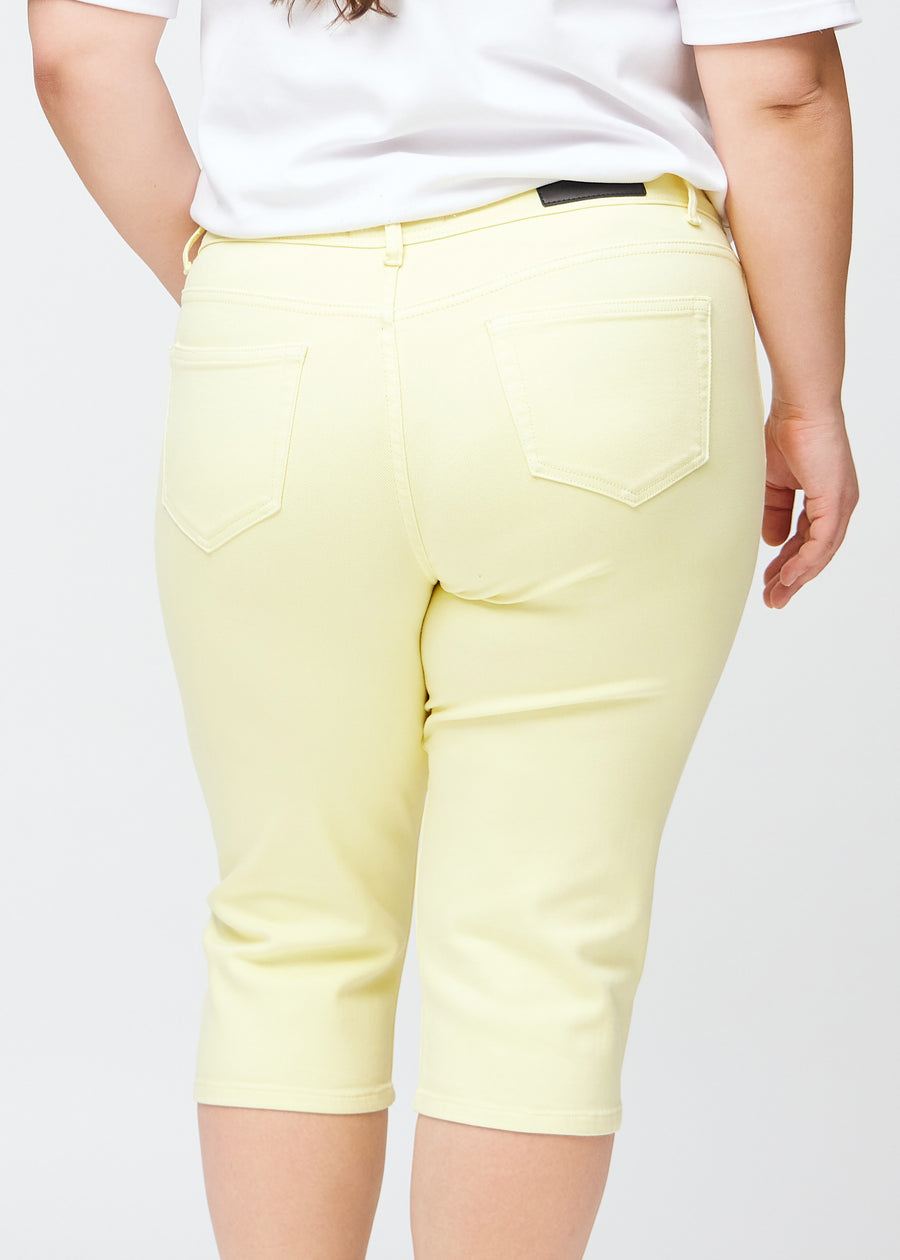 Slim capris for women in pastel light yellow jeans fabric, color Lemonades. Close-up from behind on a plus-size model, highlighting the back pockets and stitching.