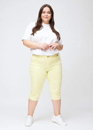 Slim capris for women in pastel light yellow jeans fabric, color Lemonades. Full-length view of a plus-size model wearing slim capris.