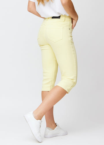 Slim capris for women in pastel light yellow jeans fabric, color Lemonades. Back view on a model, showing the fit, length and back pockets.
