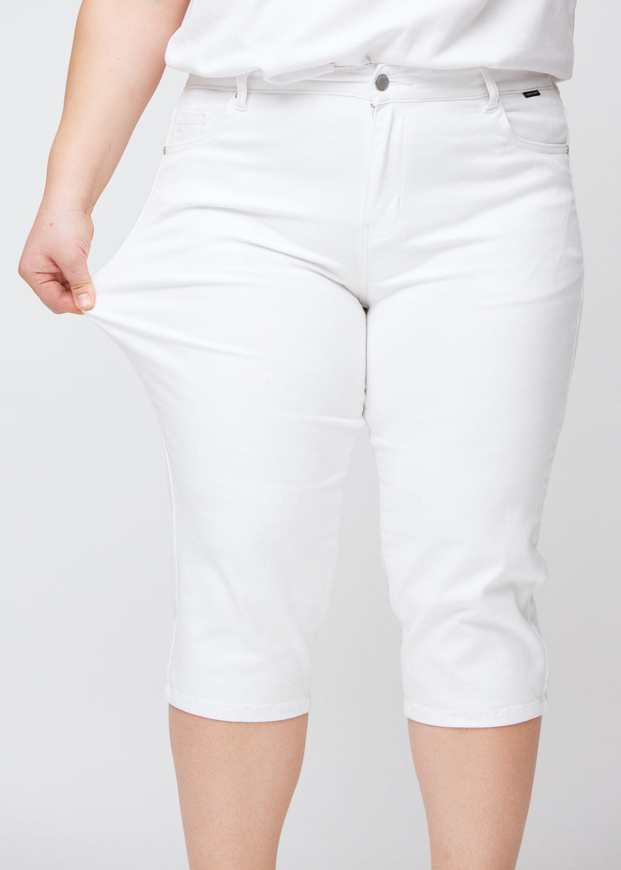 Slim capris for women in white jeans fabric, color Marguerites. A plus-size model pulls the fabric at the thigh to demonstrate stretch and flexibility.