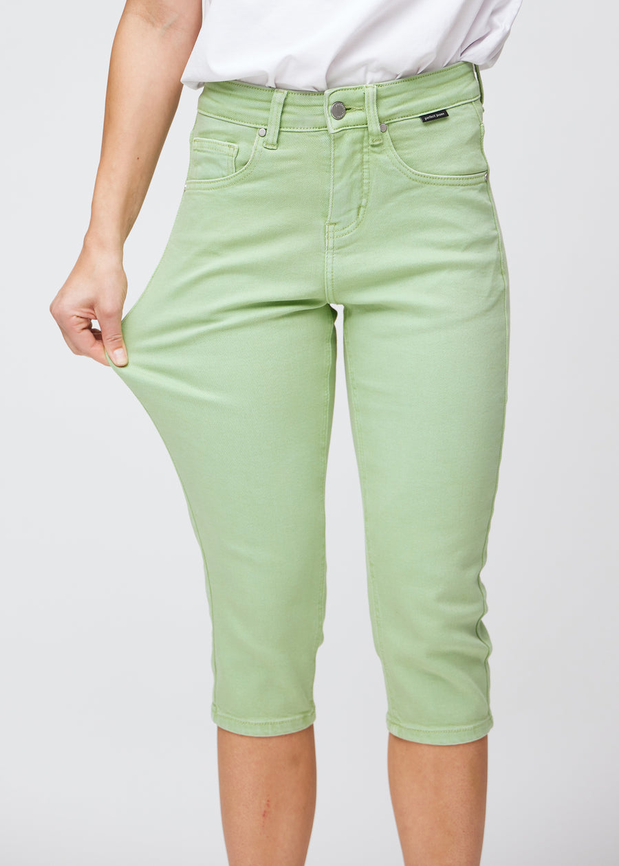 Slim capris for women in pastel light green jeans fabric, color Mints. A model pulls the fabric at the thigh to demonstrate stretch and flexibility.