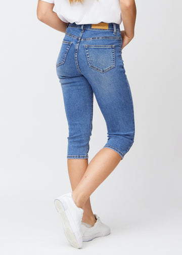 Slim capris for women in blue denim, color Rivers. Back view on a model, showing the fit, length and back pockets.