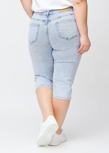 Light blue denim slim capris seen from the back on a plus-size model, clear image of the entire product and pockets.