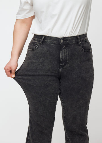 Dark grey mid-rise bootcut jeans in Shadows. A plus-size model stretches the jeans at the thigh to show the fabric&