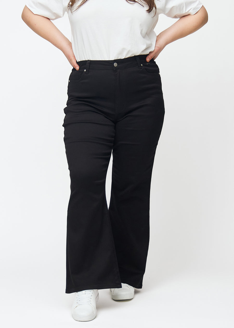 Black high-waisted bootcut jeans, model name Ravens, which fit closely from the waist to the thigh and have a slight flare at the bottom, on a plus-size model, seen from the front.