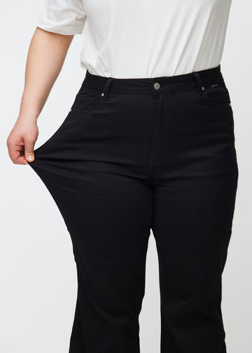 The plus-size model stretches the jeans at the thigh to show the stretch.