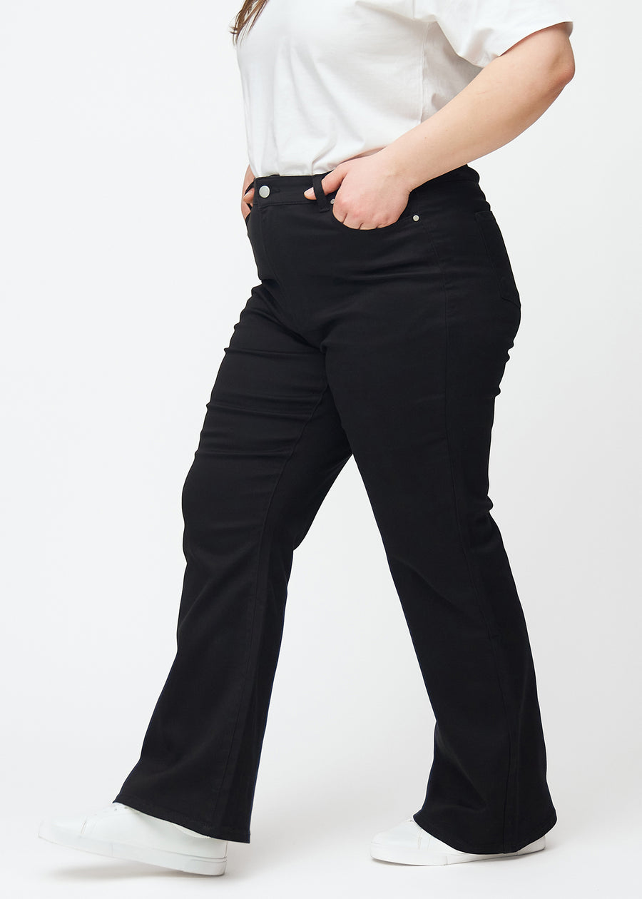 Black high-waisted bootcut jeans seen from the side on a plus-size model.