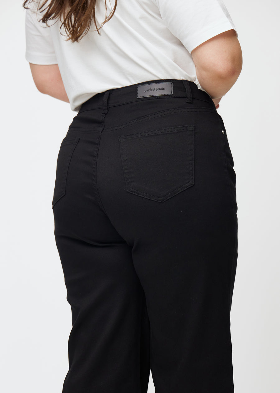 Black high-waisted jeans, which are fitted at the waist and have a loose fit with width down the leg, shown close up from the back on a plus-size model to show details.