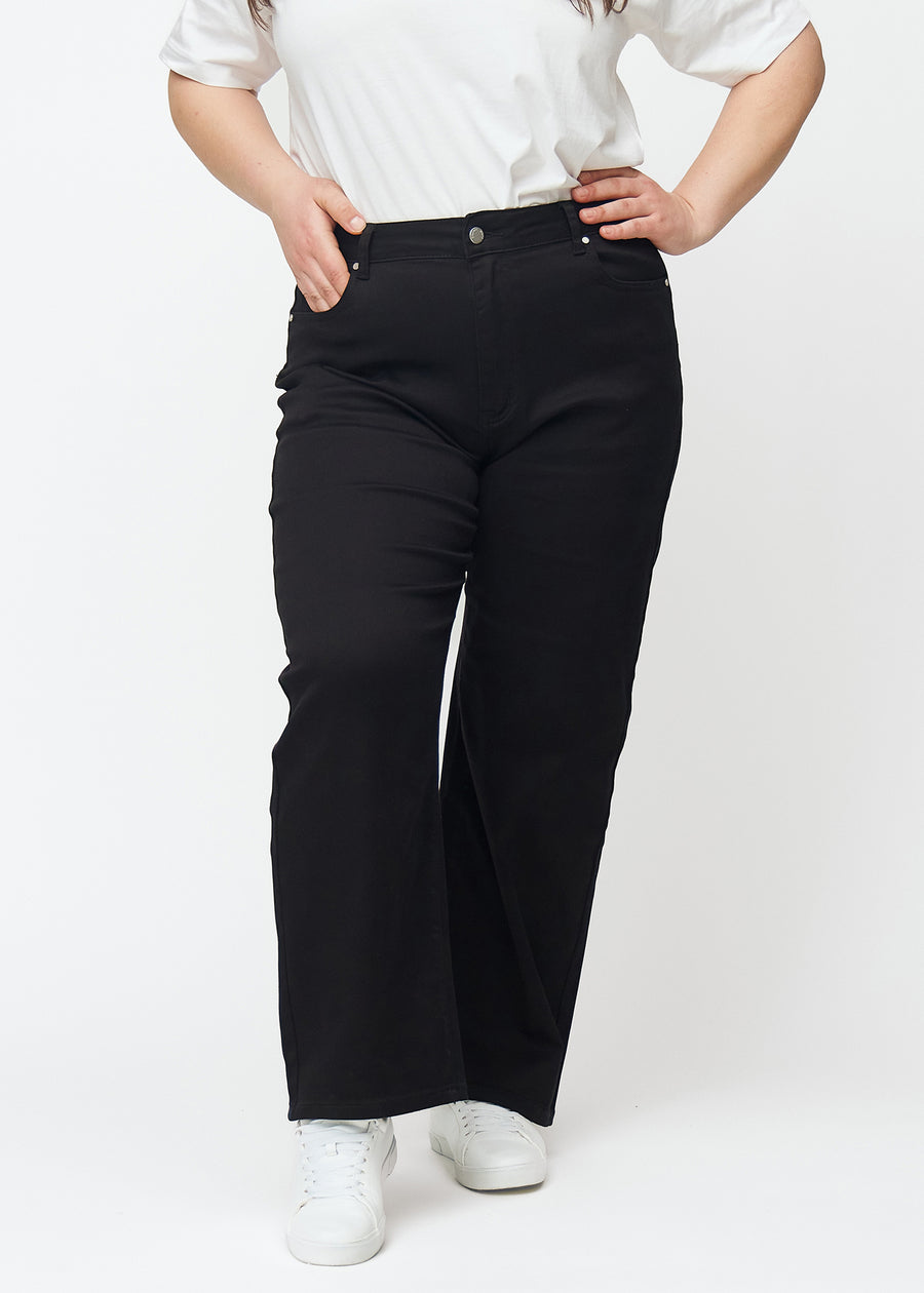 Black high-waisted jeans in the Ravens model, which are fitted at the waist and have a loose fit with width down the leg, on a plus-size model shown from the front.
