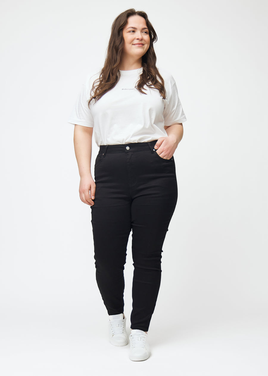 This is a full image of a plus size model wearing black high rise skinny jeans for women in the color Ravens.