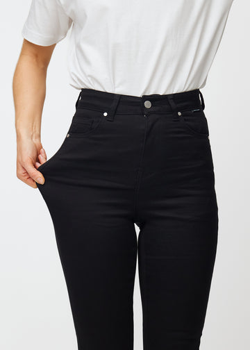 A model stretches the black Ravens stretch jeans with a high waist to illustrate the fit.