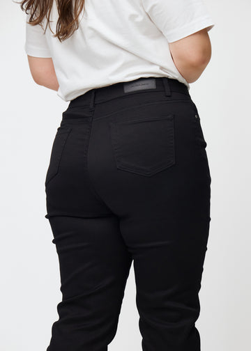 Black high-waisted slim jeans seen from the back close up on a plus-size model to show details.