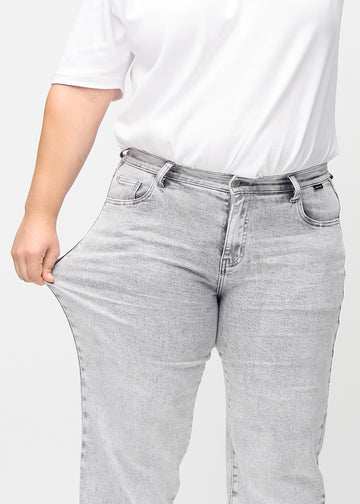 Loose jeans for women in light grey, color Ashes. A plus-size model stretches the denim at the thigh to show the fabric&