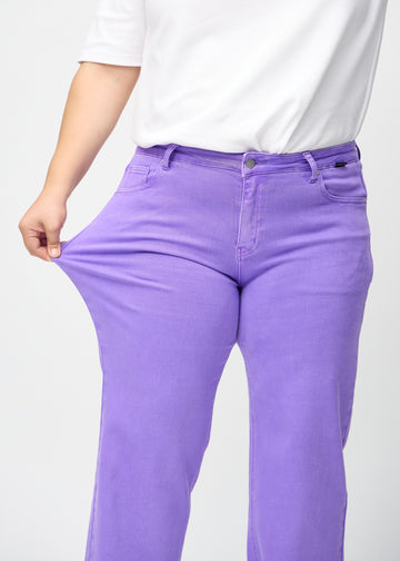 Loose jeans for women in purple, color Lavenders. A plus-size model stretches the denim at the thigh to show the fabric&