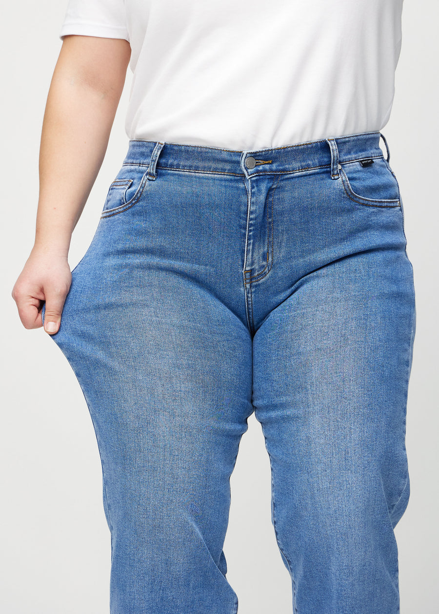 Loose jeans for women in blue, color Rivers. A plus-size model stretches the denim at the thigh to show the fabric&