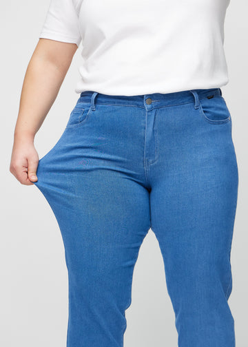 Regular jeans for women in blue, color Geraniums. A plus-size model stretches the fabric at the thigh to show its stretch.