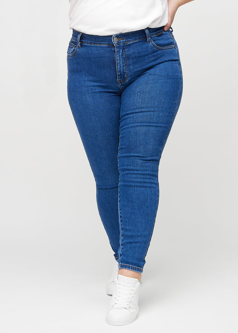 Dark denim skinny jeans, model name Oceans, which fits tightly along the leg on a plus-size model, seen from the front.