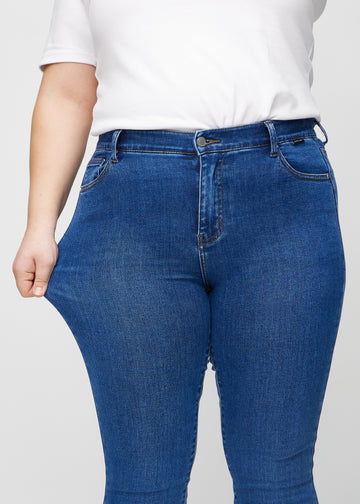 The plus-size model stretches the jeans at the thigh to show the stretch.