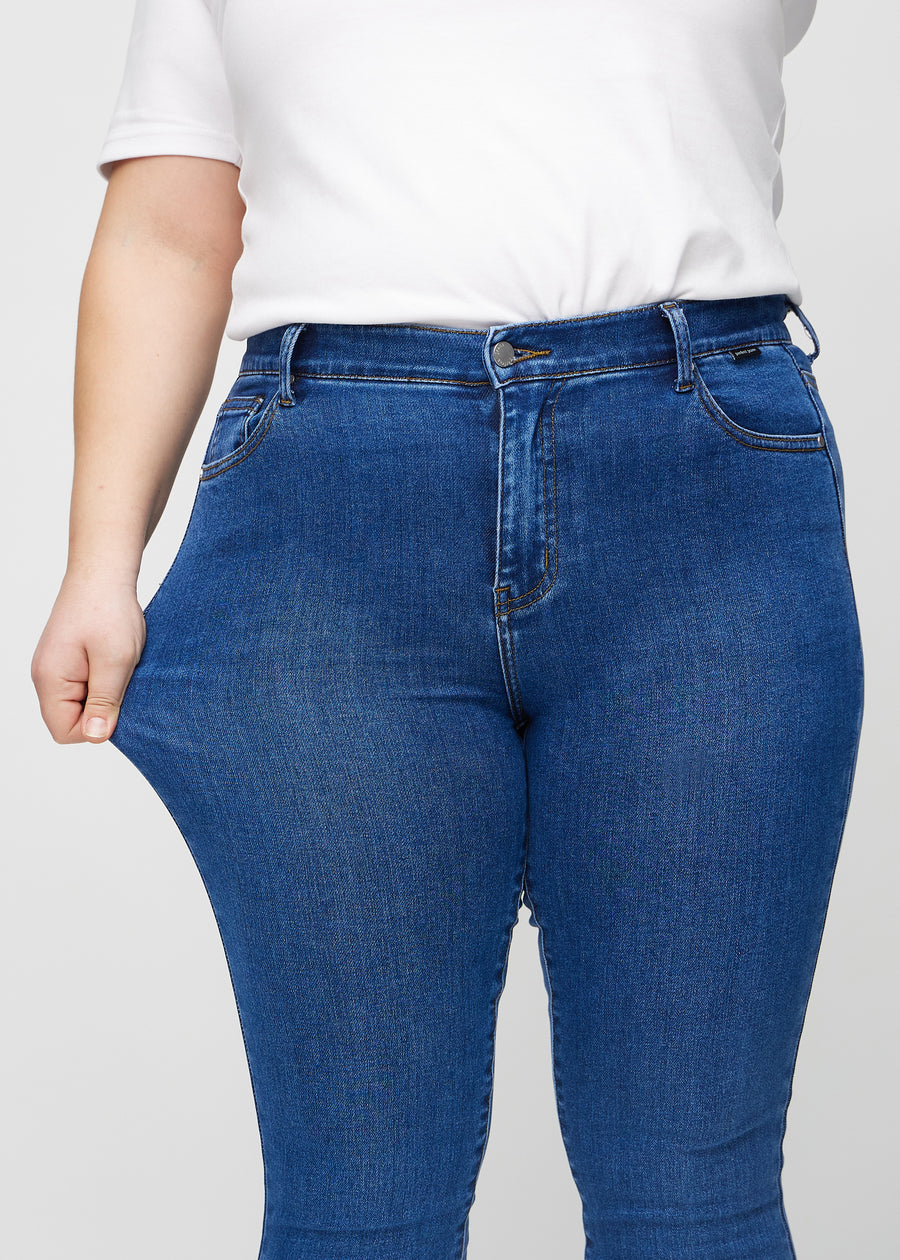 The plus-size model stretches the jeans at the thigh to show the stretch.