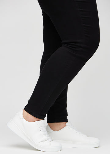 Skinny jeans for women in black, color Ravens. Close-up at the ankles on a plus-size model, showing the close-fitting leg openings.