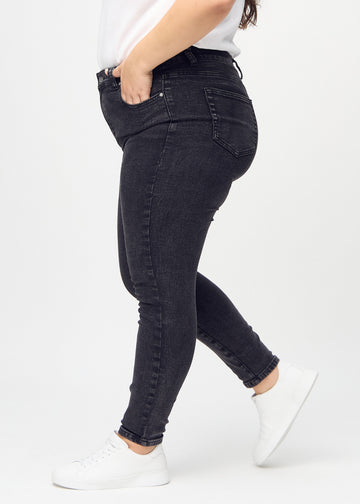 Dark grey denim skinny jeans seen from the side on a plus-size model.