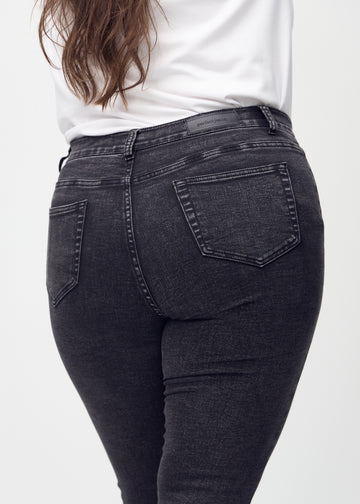 Dark grey denim skinny jeans seen from the back close up on a plus-size model to show details.