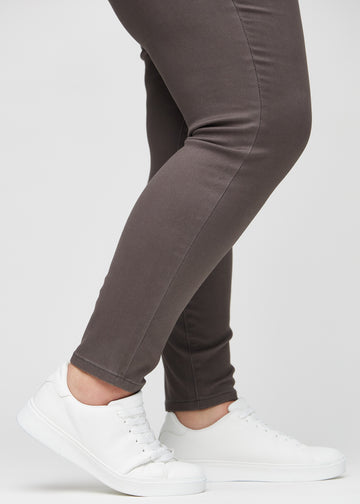 Skinny jeans for women in grey brown, color Thunders. Close-up of the snug-fitting leg openings at the ankles on a plus-size model.