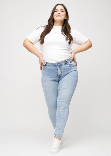 Skinny jeans for women in light blue, color Waves. Full-length view of a plus-size model in the jeans.