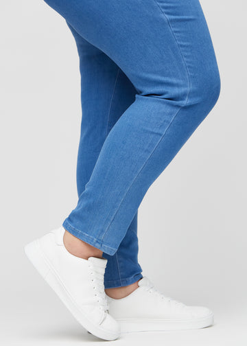 Slim jeans for women in blue, color Geraniums. Close-up at the ankles on a plus-size model, showing the fit at the leg openings.