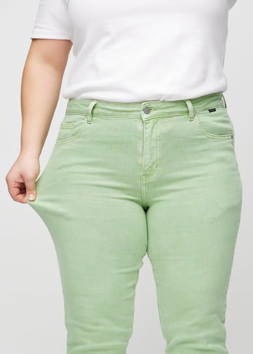 Slim jeans for women in light green, color Mints. A plus-size model stretches the jeans at the thigh to show the fabric&